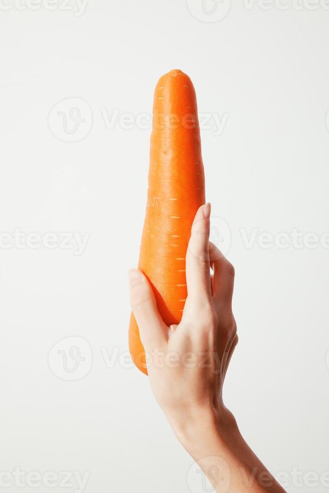Person holding up fresh carrot against a white background. copy space available for text or logo photo