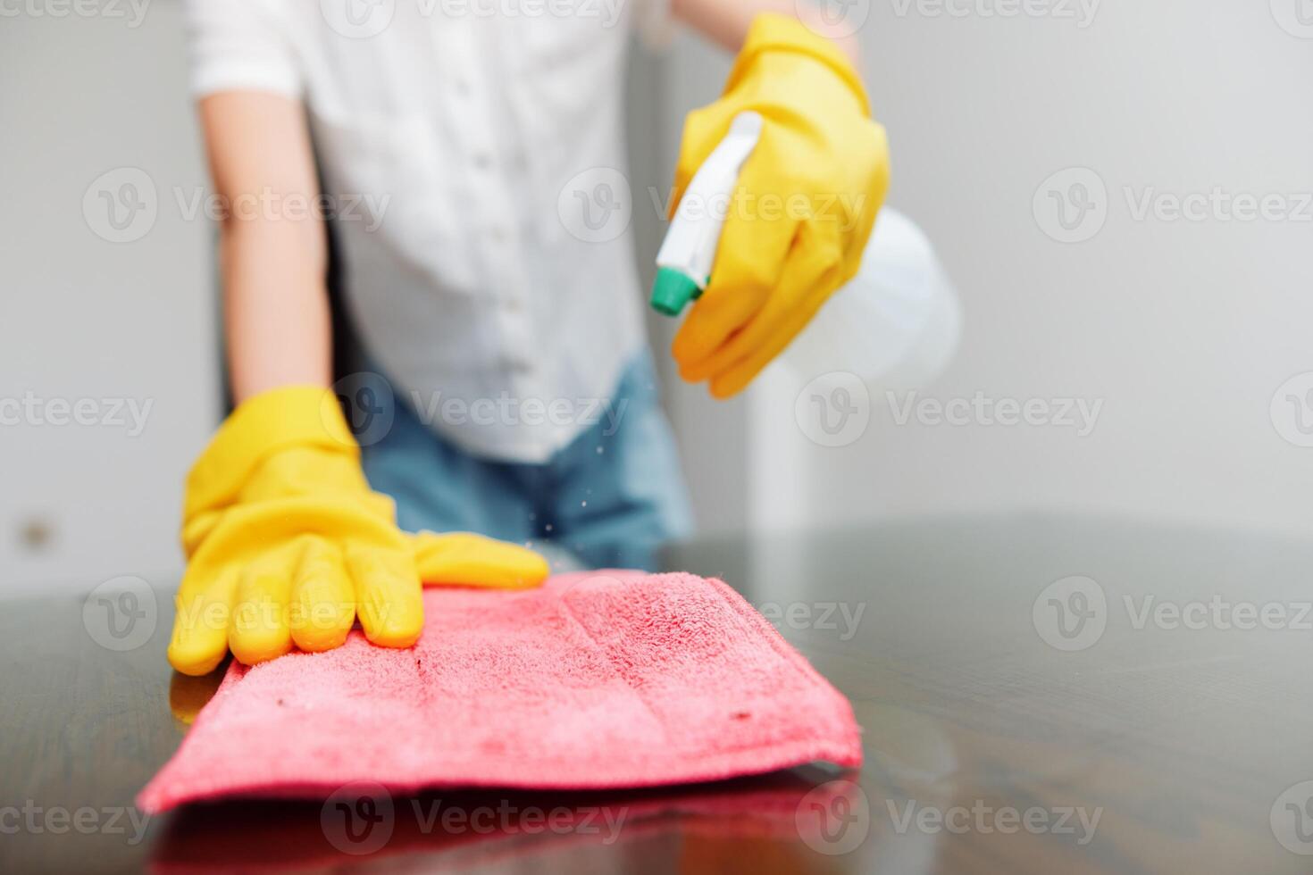 Cleaning woman in yellow gloves wiping table with rag and using solution bottle. photo