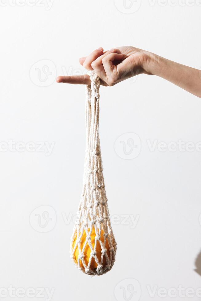 White macrame bag with orange details being held by a person against a white background. photo