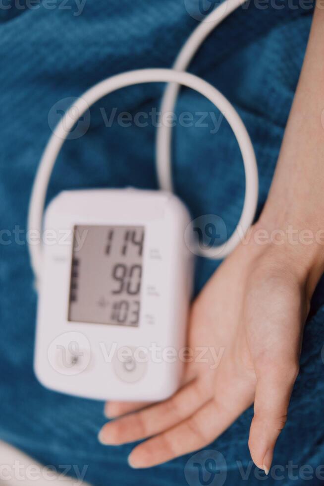 Person holding blood pressure monitor, sitting on bed with arm up. digital monitor on bed next to photo