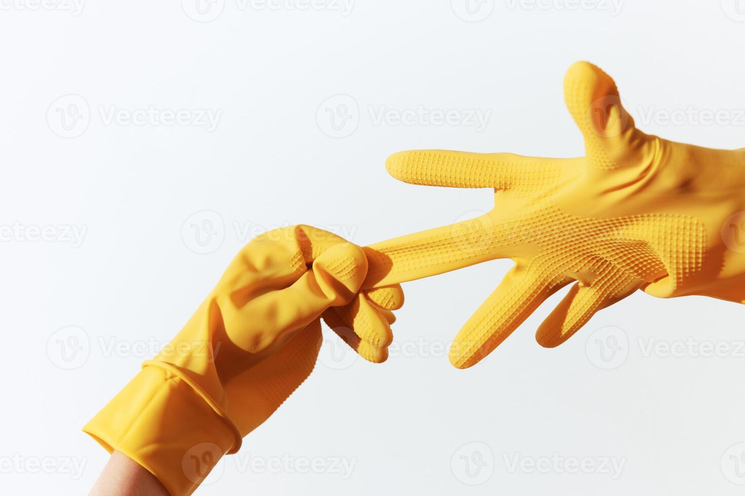 Two people wearing yellow rubber gloves reaching out to each other on a white background. photo