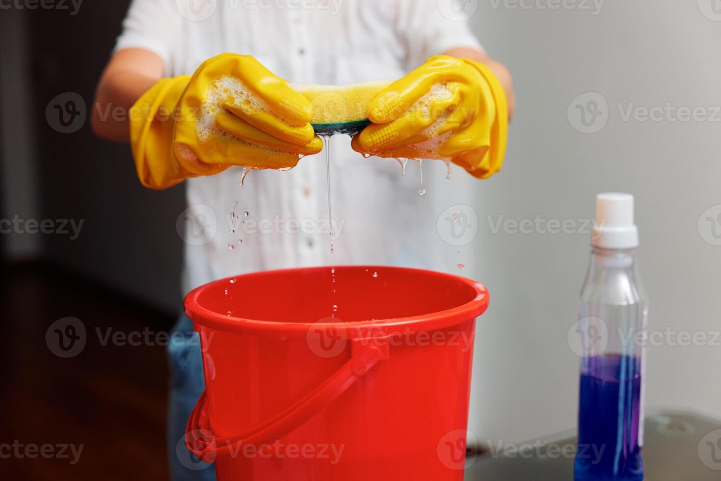 Woman wearing rubber gloves holding a sponge over a red bucket with cleaning solution and hand photo