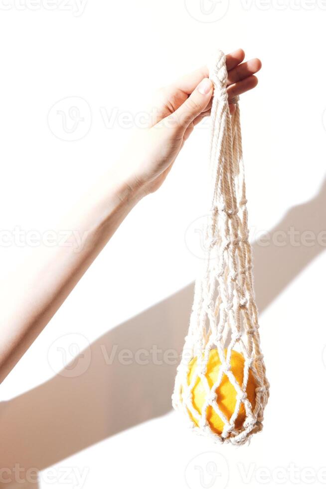 Caucasian person holding white cotton net bag with orange fruit inside, isolated on white background photo