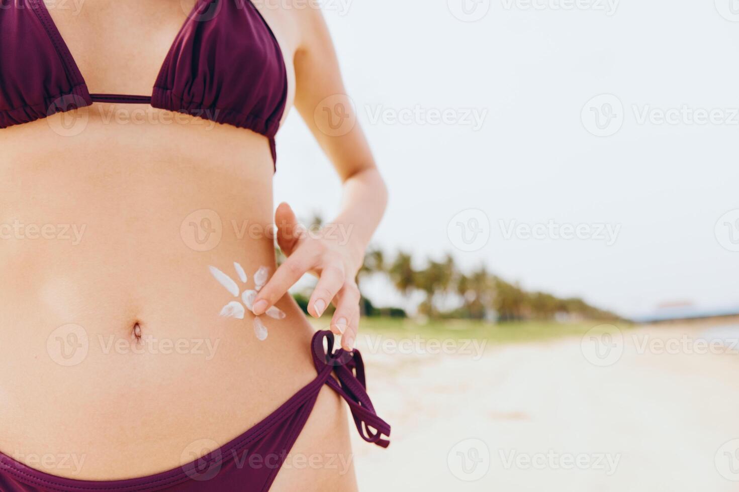 Young woman in purple bikini standing confidently on a sandy beach with hands on hips, showcasing a photo