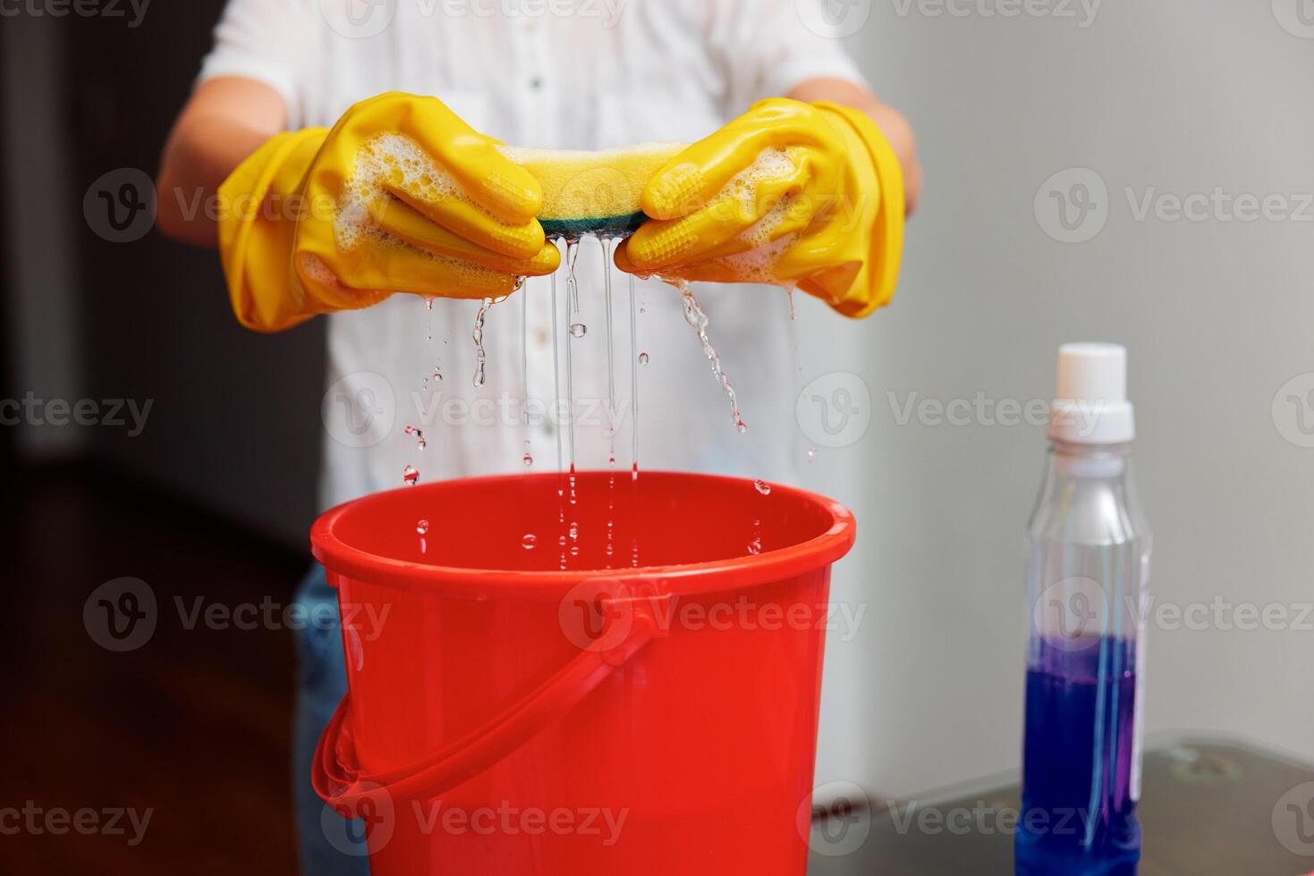 Woman in yellow gloves washing bucket with cleaning solution in front of red bucket. cleaning photo