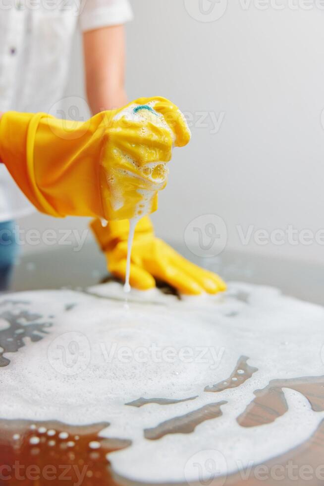 Cleaning woman in yellow rubber gloves cleaning table with sponge and soap on wooden surface. a photo