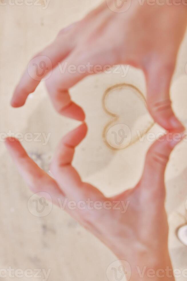 Hands making heart shape with sand on white countertop, holding pair of scissors. photo