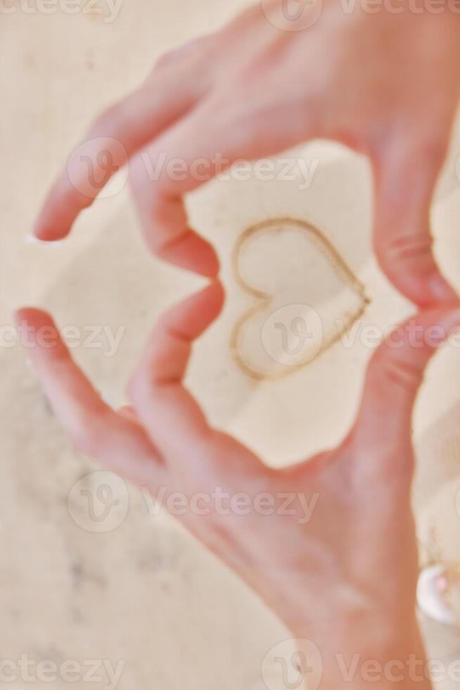 Hands making heart shape with sand on white countertop with ocean view through window. photo