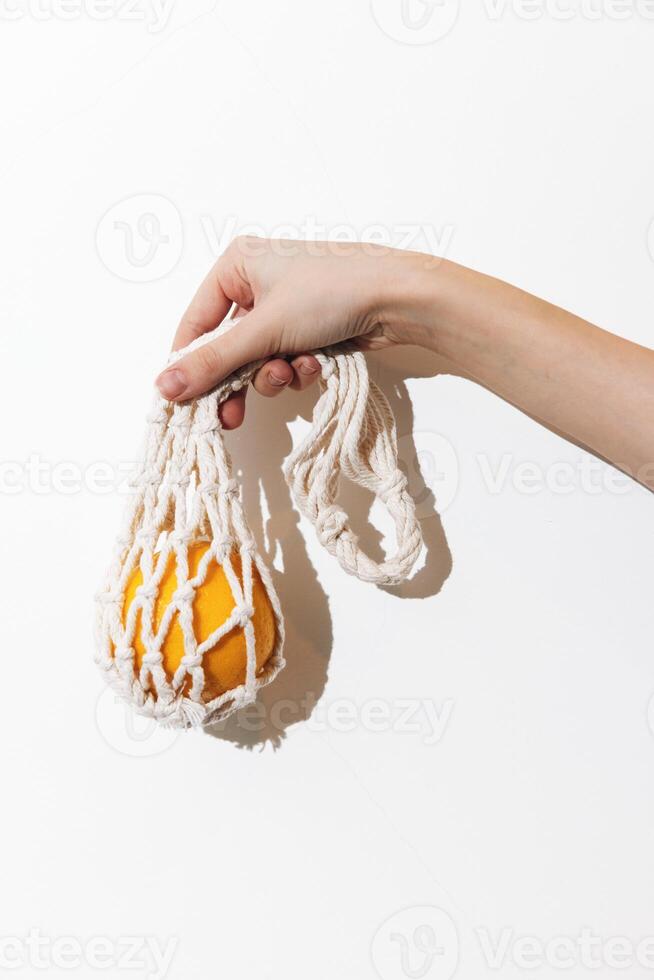 Female hand holding white net bag with orange fruit on a white background. a fresh and eco-friendly photo