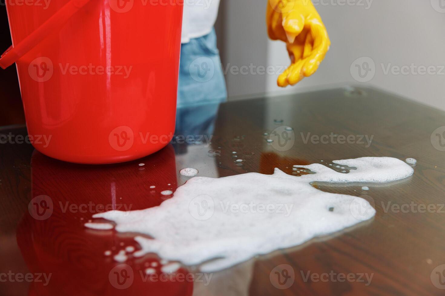 Woman cleaning table with soapy water bucket and red bucket nearby. a woman is cleaning a table with photo