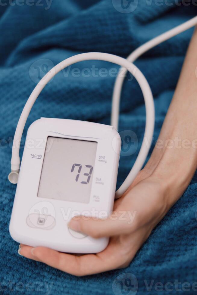 A person is holding an electronic blood pressure monitor on a blue blanket next to a person laying photo