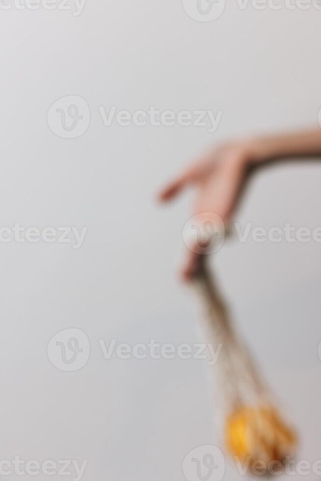 Man holding an orange fruit attached to a rope, standing in front of a white wall with a clear blue photo