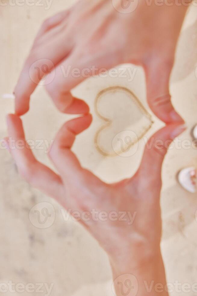Hands forming heart in sand with feet on ground. romantic gesture on beach. love and connection photo