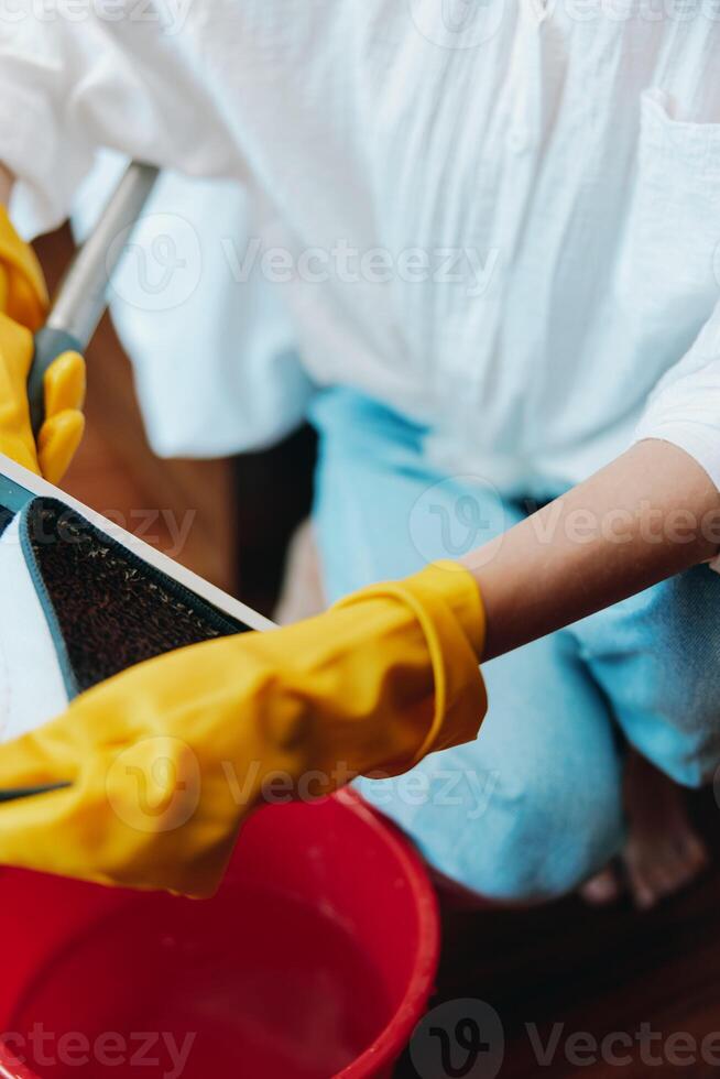 Cleaning woman in yellow gloves wipes red bucket with sponge and mop on wooden floor in front of photo