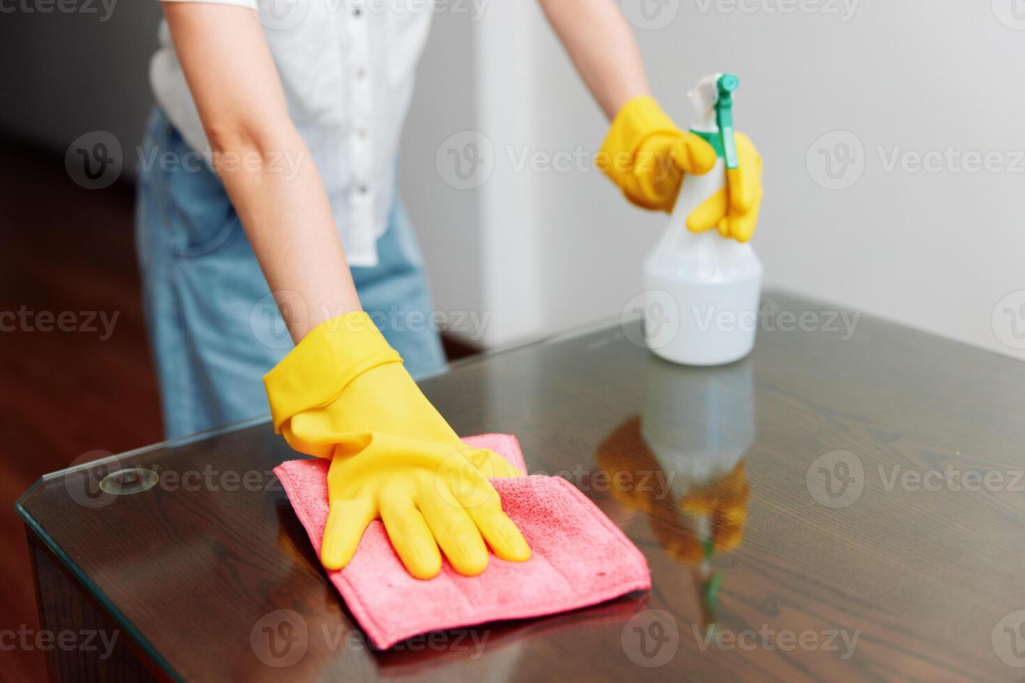 Woman in yellow gloves cleaning table with rag and cleaning solution bottle. photo