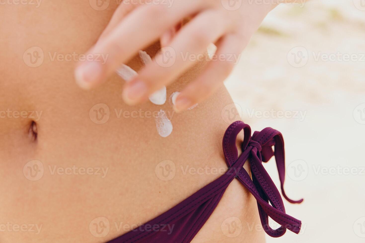 Young woman in a purple bikini applying lotion to her skin, with small white objects placed on her photo