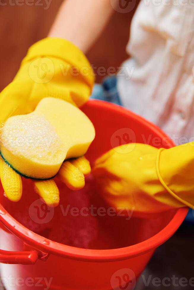 Yellow gloves woman holding sponge in red bucket with yellow sponge inside. photo