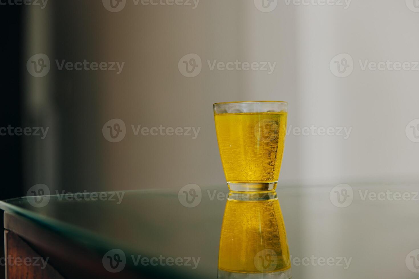 Glass of yellow liquid on table with white wall and black door in background. photo