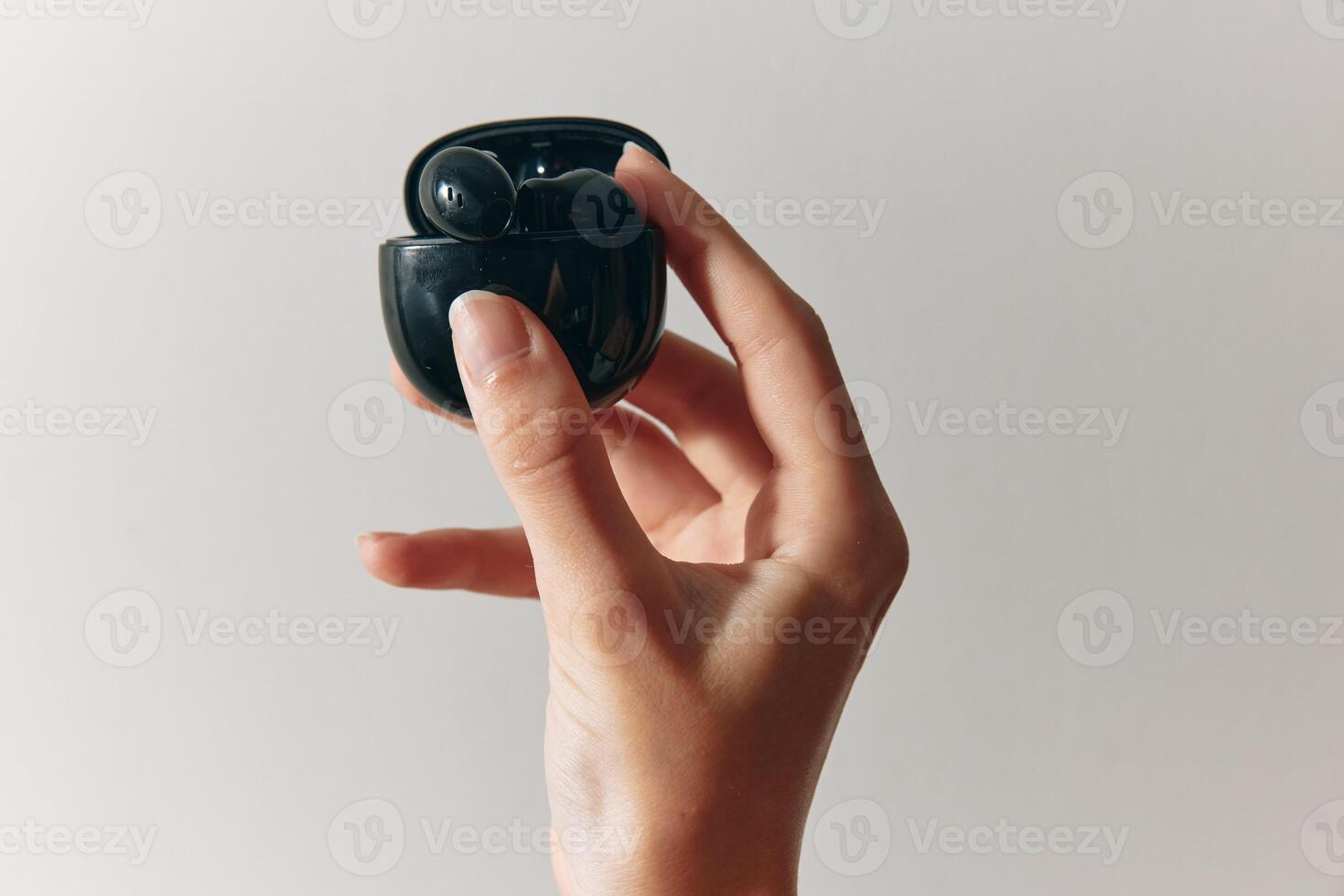 Earbud and small black device held by a person against a white background. photo