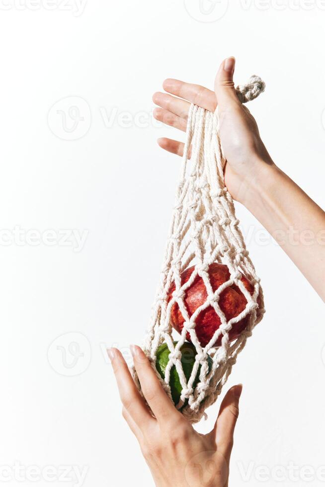 Person holding a white net bag filled with green and red apples on a white background. photo