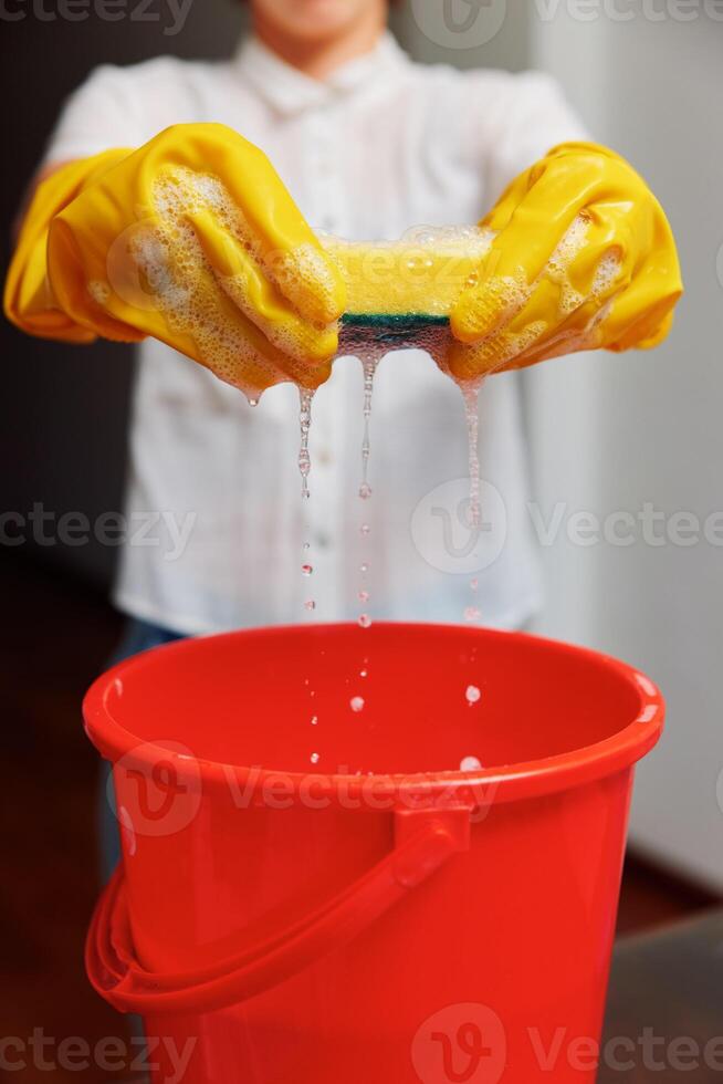 Woman in yellow rubber glove holding sponge over red bucket with water flowing out. cleaning concept photo