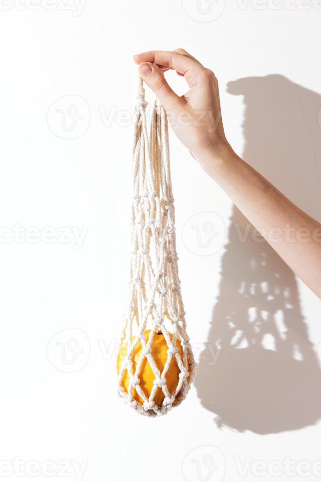 Macrame bag in white color being held by a person's hand, with an orange accent and a shadow cast on photo