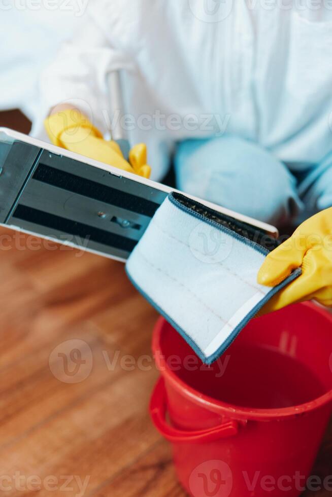 Person wearing yellow rubber gloves holding a tablet next to a bucket with red bucket on the floor. photo