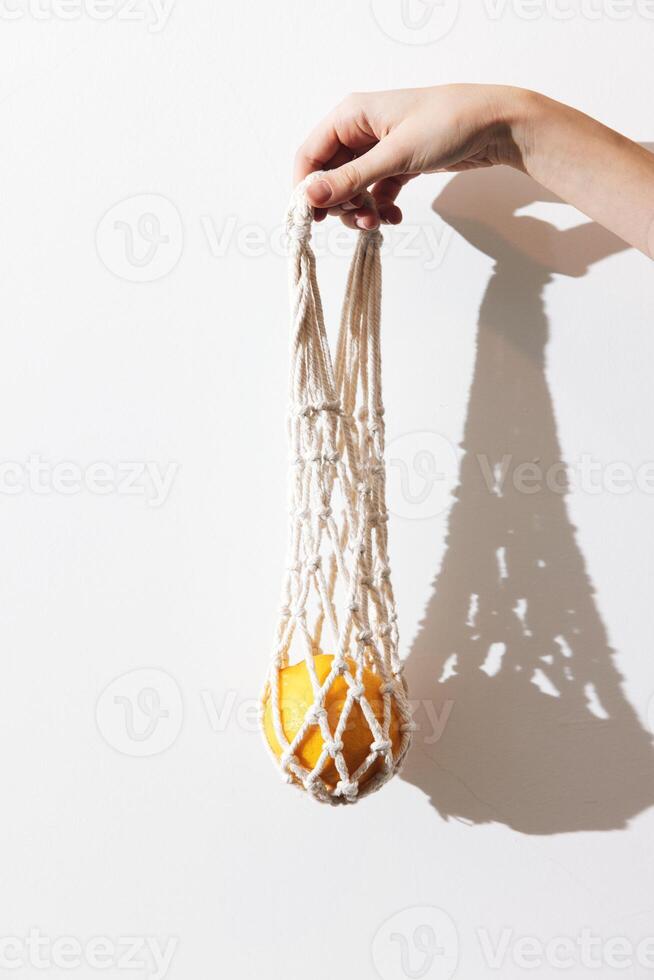 Macrame bag with white exterior and orange interior being held by a person against a white wall with photo