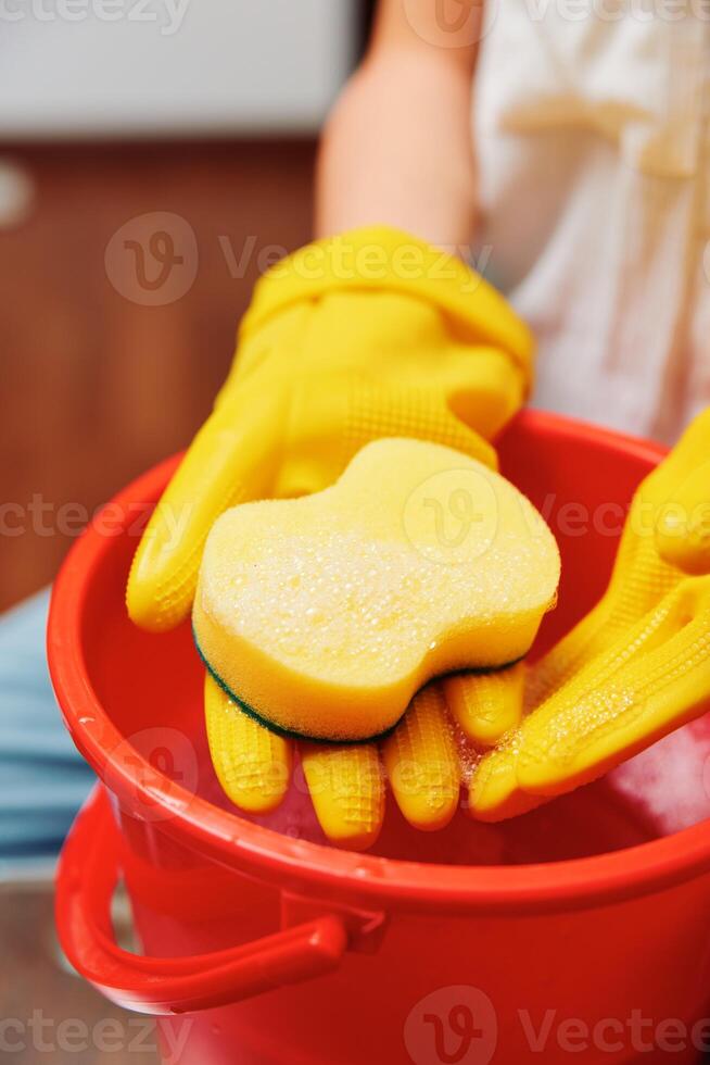 Woman in yellow gloves holding sponge in red bucket filled with yellow sponges. photo