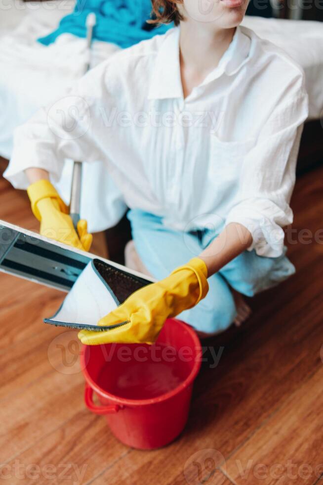 Woman in yellow gloves holding a tablet, sitting by a bucket of water. photo