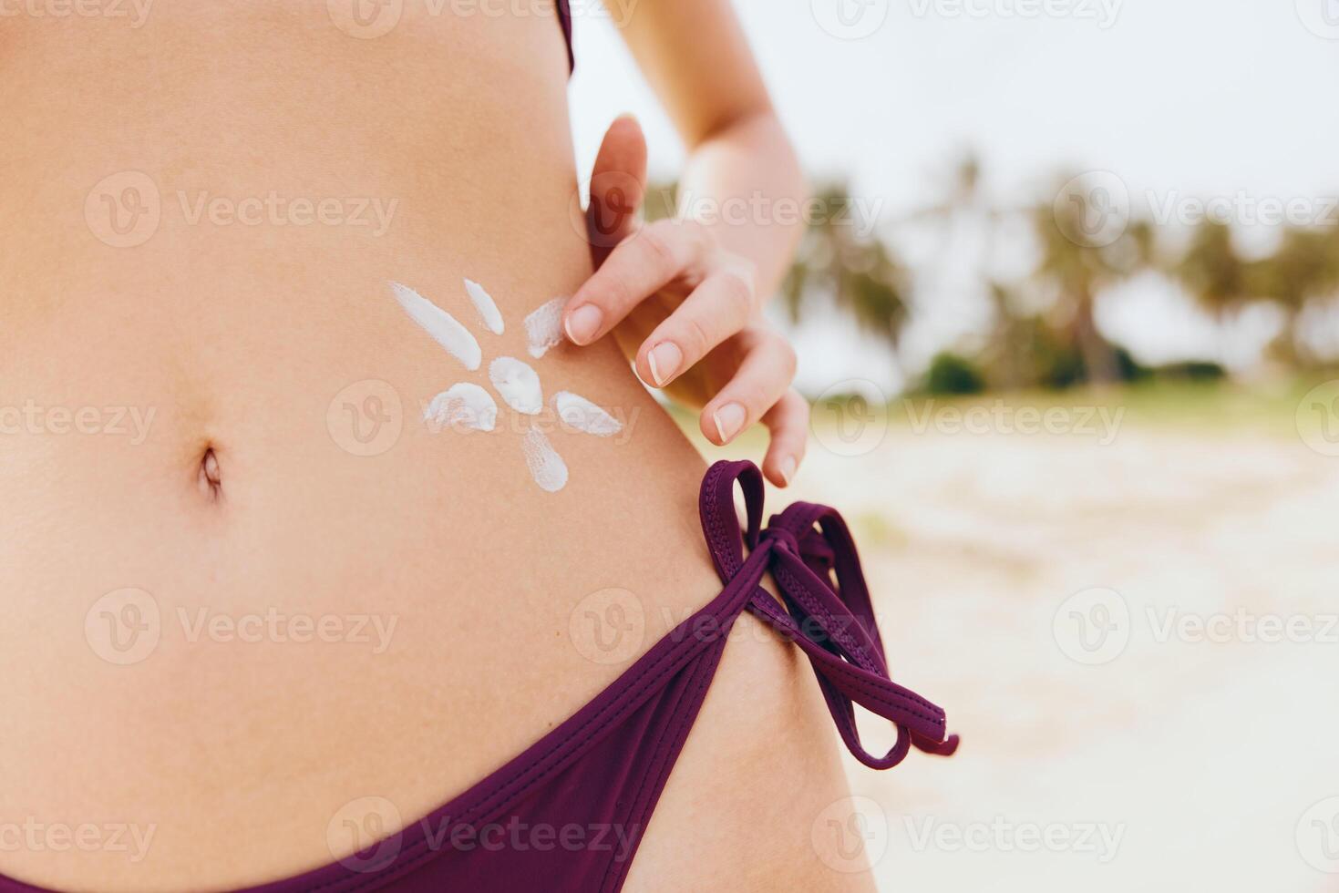 Woman applying sunscreen on her body in front of a palm tree wearing a bikini. photo