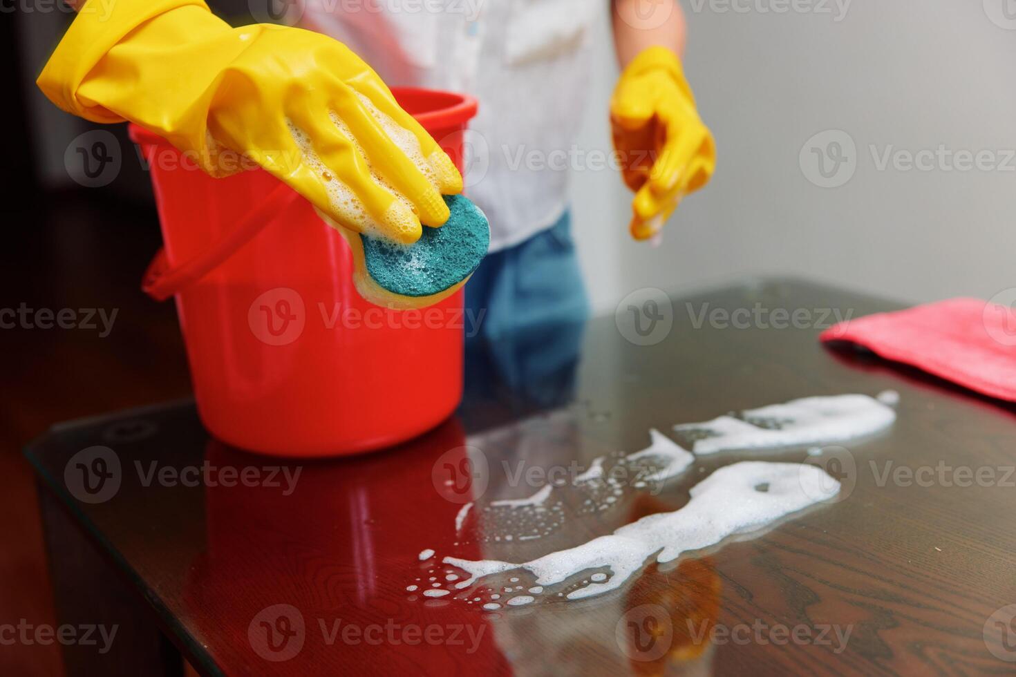 Woman cleaning table with soapy water and sponge, red bucket on table. photo