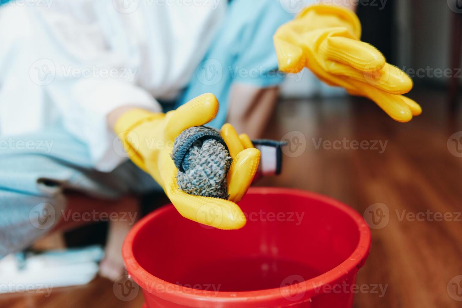 Person wearing rubber gloves holding a rock in a bucket, with a red bucket nearby, on a wooden floor photo