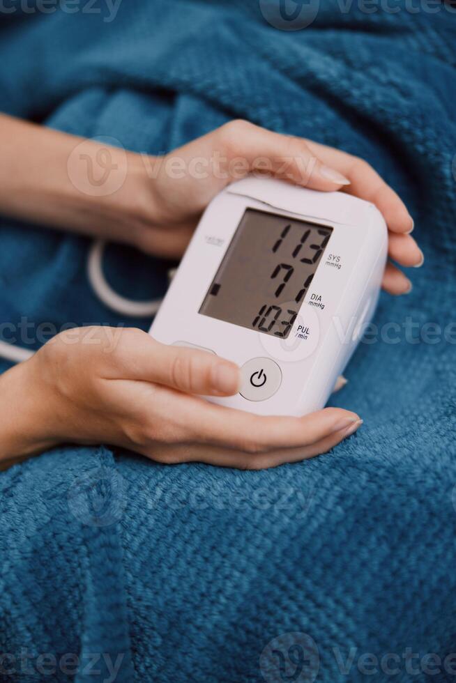 Hand holding electronic blood pressure monitor while laying on blue blanket with arm in air. photo