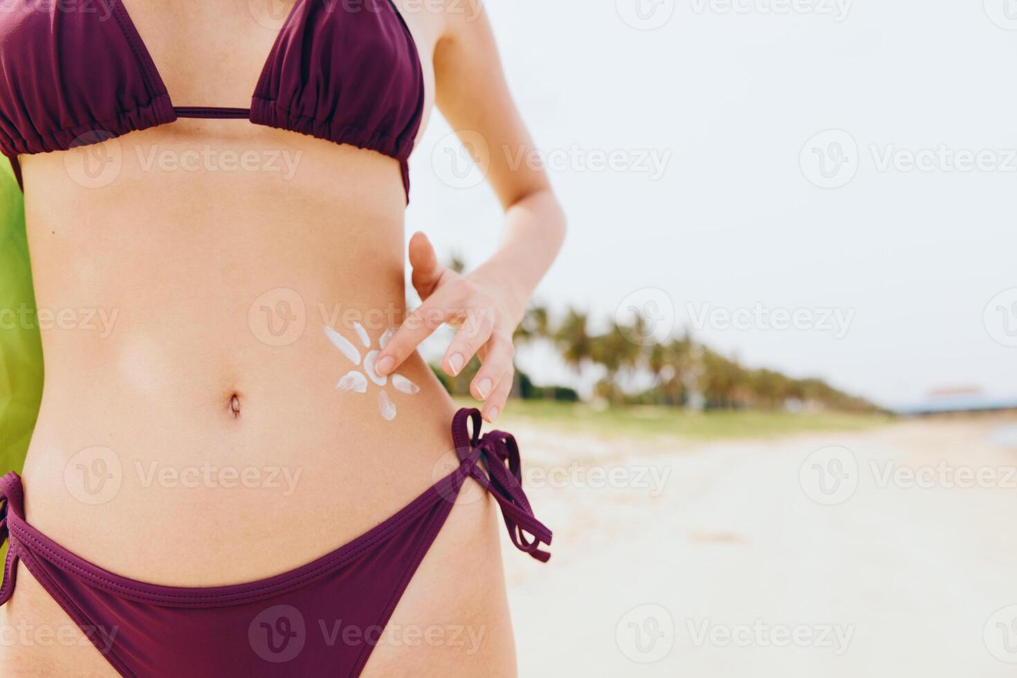 Woman in bikini standing on beach with white sticker on stomach and towel around neck. photo