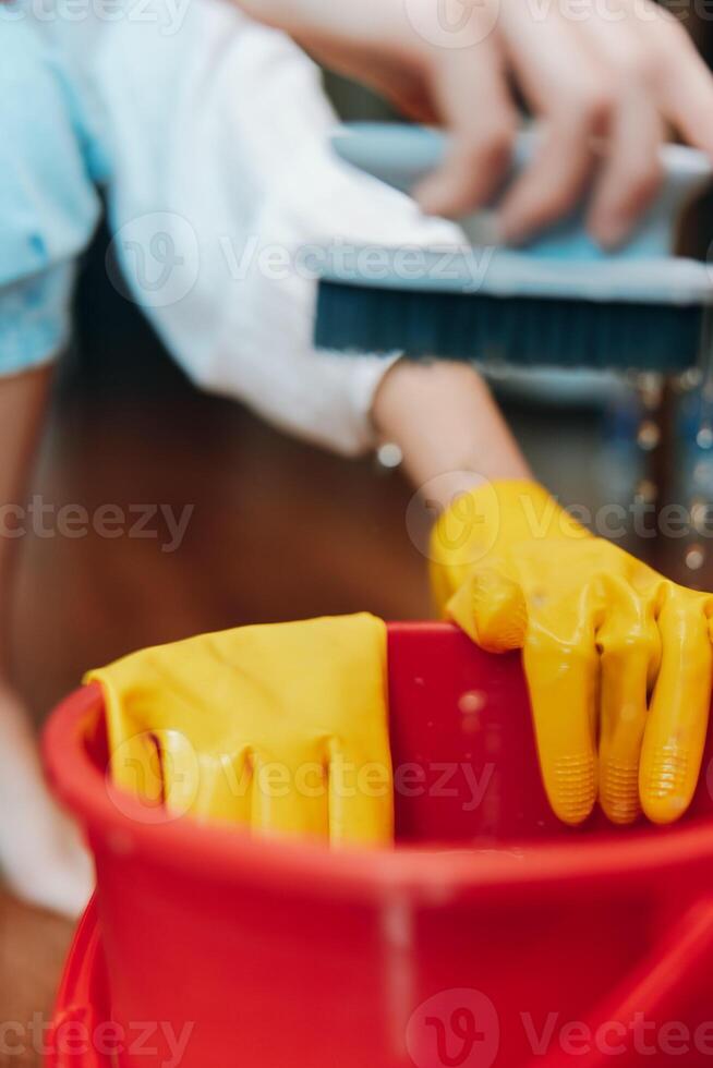 Cleaning person wearing yellow rubber gloves scrubbing a red bucket with a brush on wooden floor photo