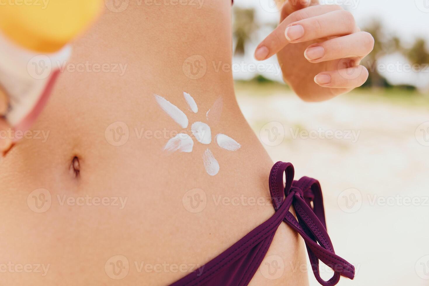 Woman in bikini applying sunscreen on her body while standing on the beach with a flower painted on photo