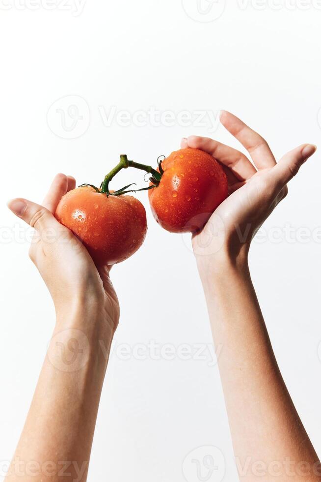 Two hands grip two ripe red tomatoes against a plain white background. a simple and fresh image photo