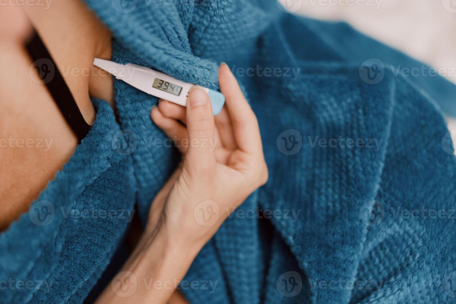 Woman with electronic thermometer wrapped in blue blanket, wearing blue shirt and bra. photo
