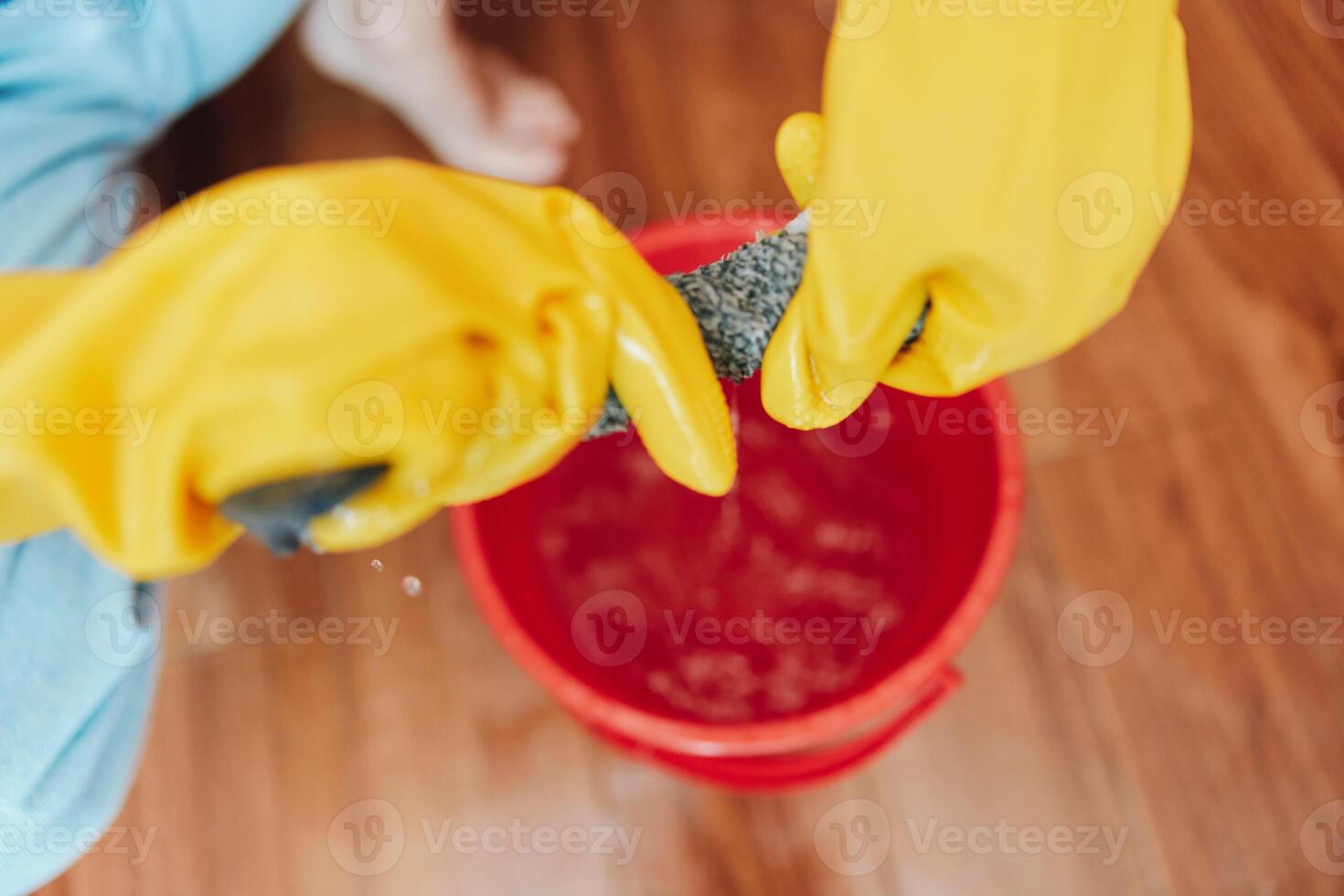 Person cleaning floor with mop and bucket of water in front of another person. one wearing rubber photo