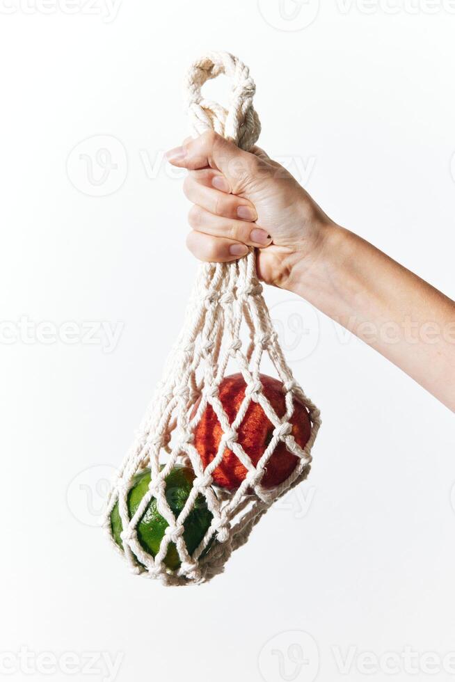 Hand holding white net bag with red and green peppers on white background. photo