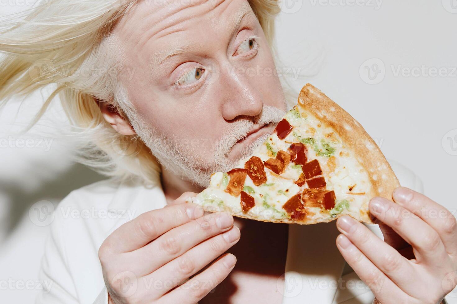 A man with blonde hair and a surprised expression is holding a slice of pizza close to his face, set photo