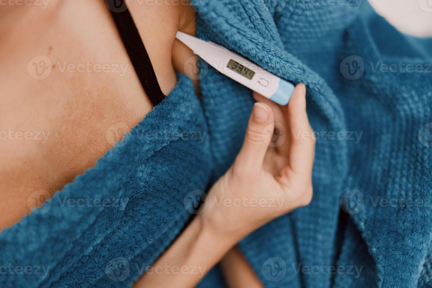 Woman holding electronic thermometer wrapped in blue towel, wearing black bra and tank top. photo