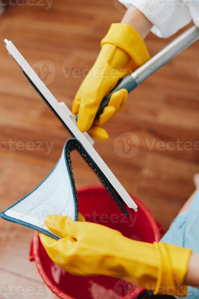 Cleaning person in yellow gloves mopping the floor in front of a red bucket with a cloth. photo