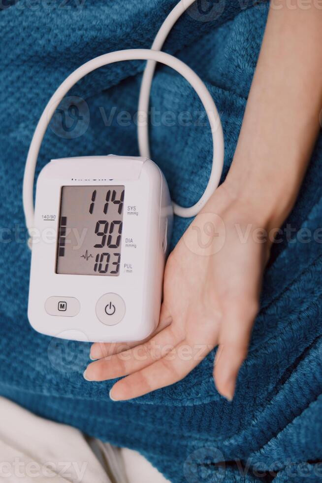 Person holding electronic blood pressure monitor while laying in bed with blue blanket. photo