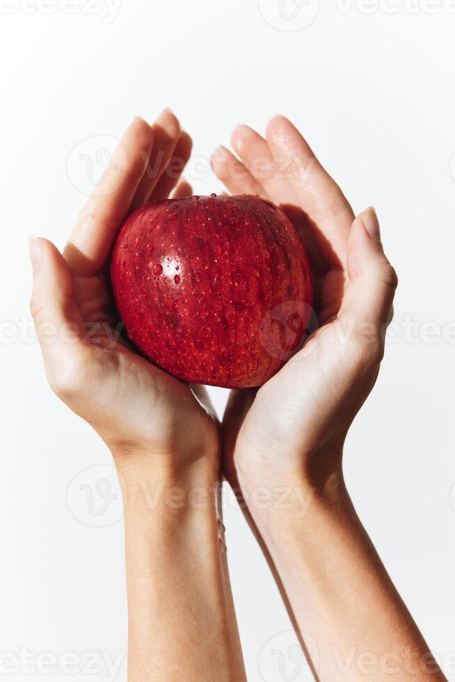Hands holding a ripe red apple against a plain white background. a simple and natural image of photo