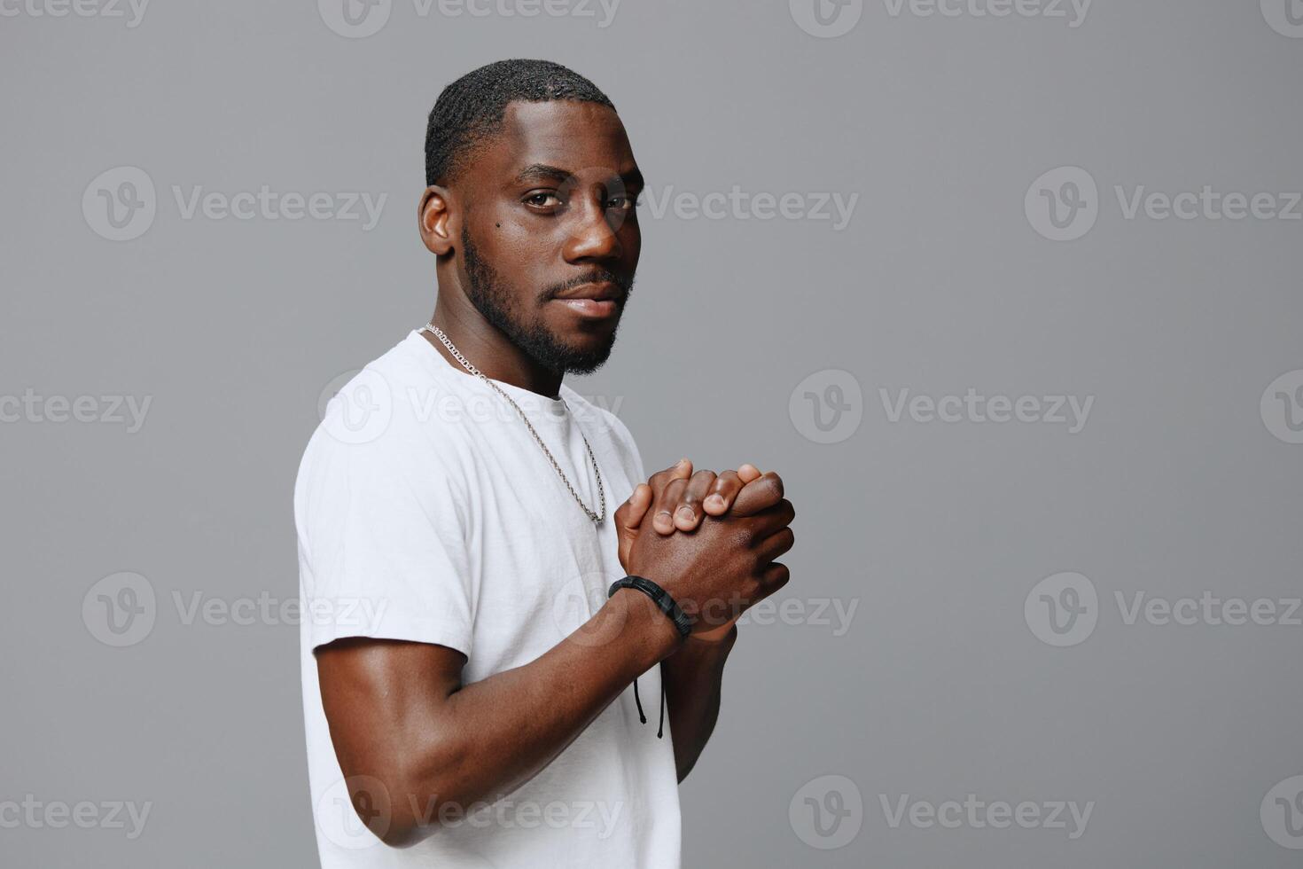 Confident young man dressed in a casual white t shirt, hands clasped together, displaying a photo