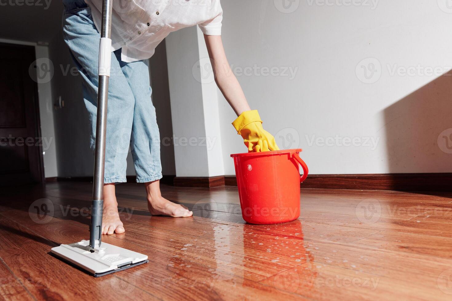 Woman cleaning hardwood floor in room corner with water bucket and mop. photo