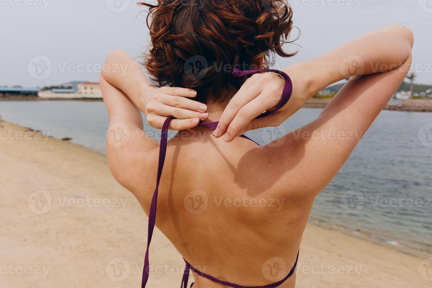 Woman in purple bikini standing on beach with hands on hips and ribbon tied around neck. photo