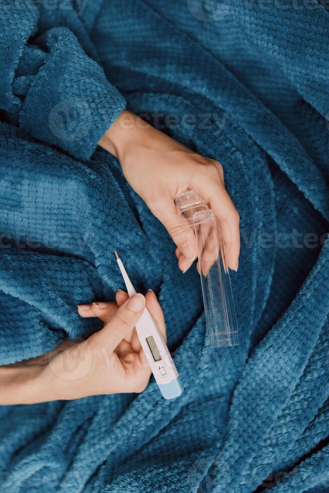 Person holding a thermometer while laying on a blue blanket with another thermometer in hand. photo